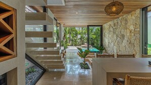 Ein modernes Interieur mit einer Treppe, die in einen Poolbereich führt, Steinwänden und einem Essbereich mit Korbmöbeln.