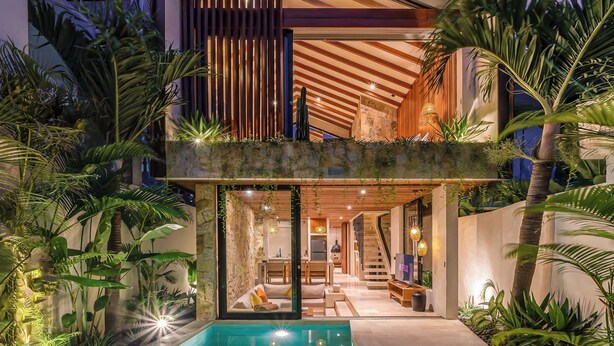 Ein modernes, zweistöckiges Haus mit Swimmingpool, Holzterrasse und tropischen Pflanzen.