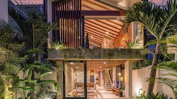 Una casa moderna de dos pisos con piscina, terraza de madera y plantas tropicales.
