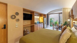 Ein Hotelzimmer mit Bett, Fernseher, einer Küchenzeile und einem Balkon mit Pflanzen.