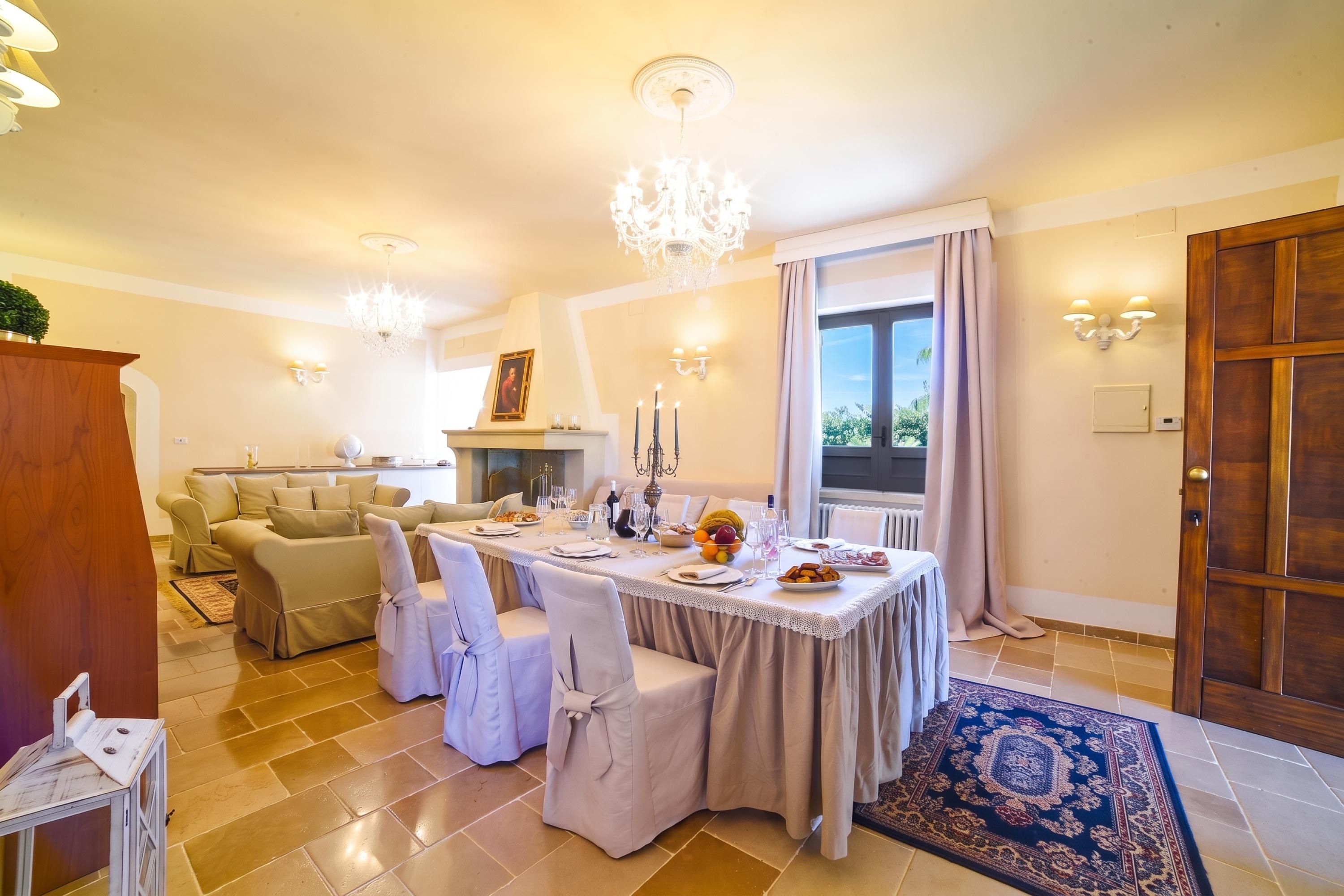 Un'area pranzo con un tavolo apparecchiato per quattro persone, un lampadario e vista all'esterno attraverso una finestra.