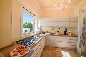 A modern kitchen with a gas stove, a sink, and a chandelier. - Villa Nina - Luxury Villa with Pool in Salento, Zollino, Italy (Zollino)