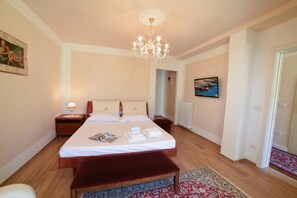 Una camera d'albergo con un letto grande, un comodino con una lampada, una panca rossa, un tappeto decorato, un quadro appeso e vista mare dalla finestra.