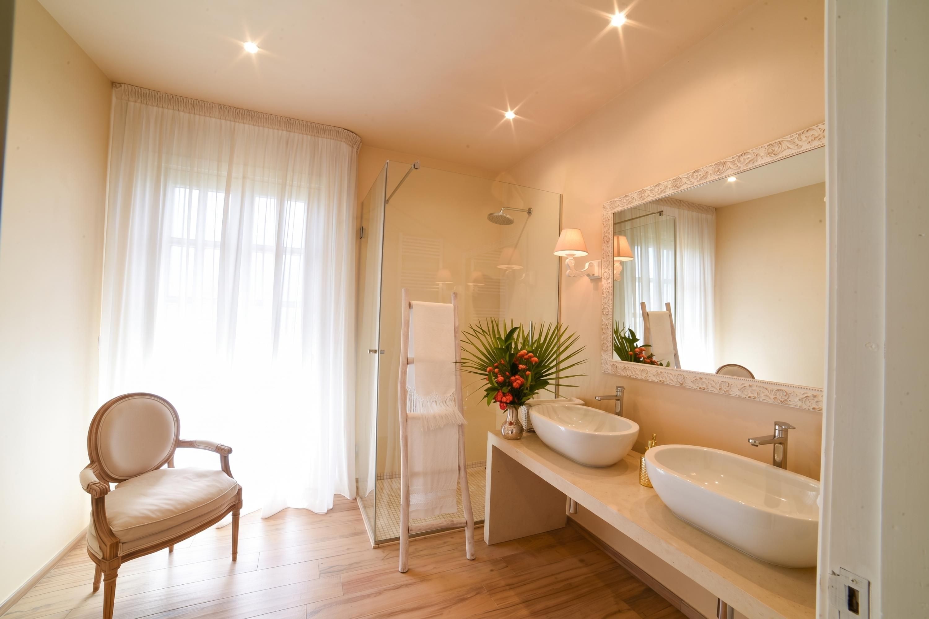 Une salle de bain avec une douche, deux lavabos, une chaise et un miroir.