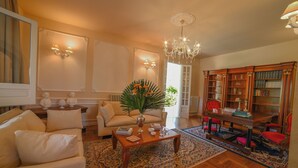 A living room with a sofa, coffee table, chandelier, bookshelf, and a large window. - Villa Nina - Luxury Villa with Pool in Salento, Zollino, Italy (Zollino)