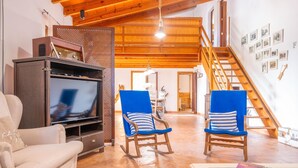 A living room with a wooden ceiling, a television, two rocking chairs, and a staircase leading to an upper level. - MIRABO - Villa with private pool and free WiFi (Manacor)