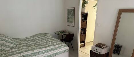 A bedroom with a bed, a desk, a chair, a bookshelf, and a mirror.