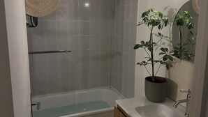 A bathroom with a bathtub, a sink, a mirror, and a potted plant.