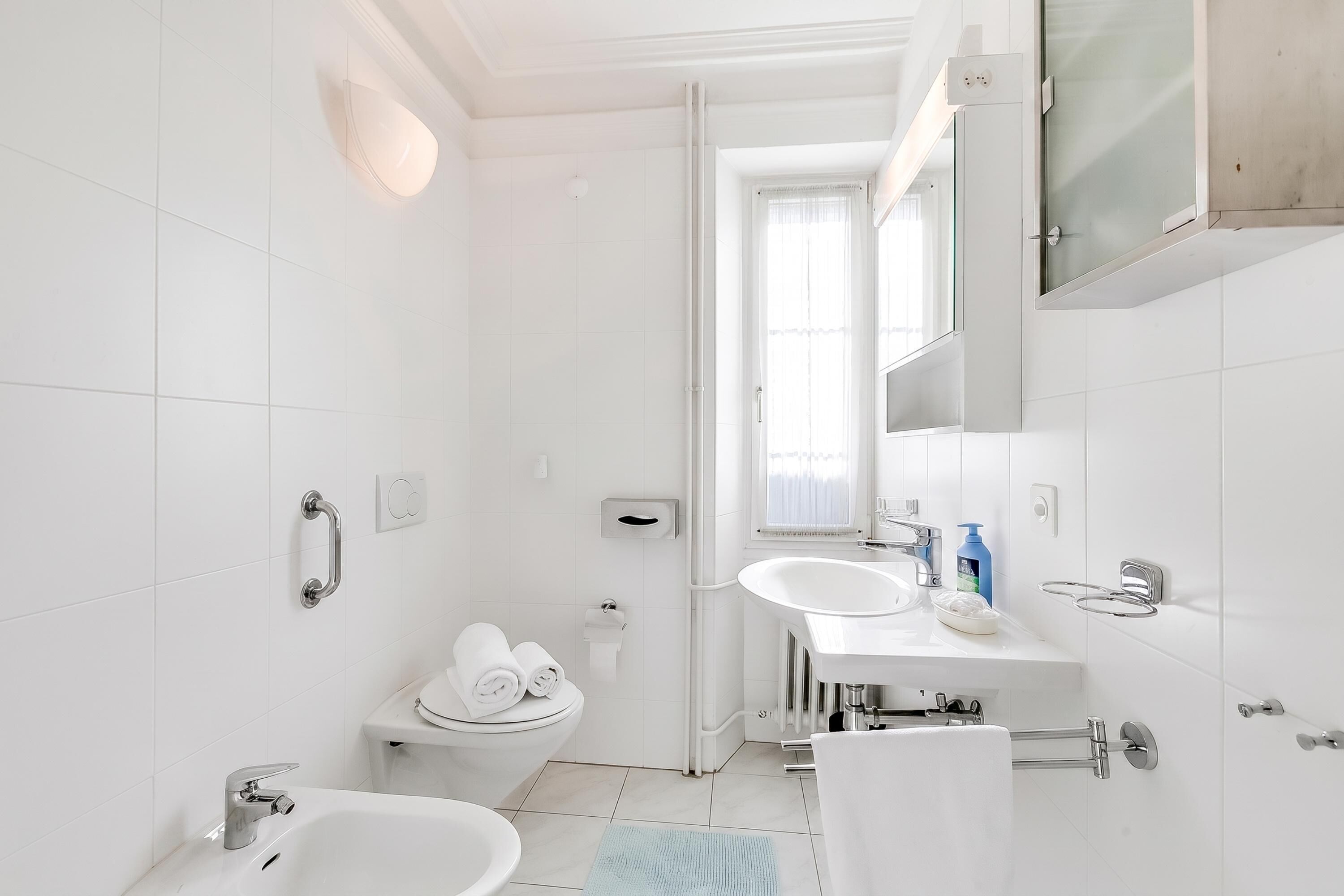 A modern bathroom with a toilet, bidet, sink, and mirror.