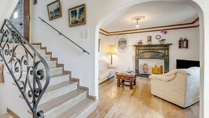 A staircase with ornate metal railings, a living room with a sofa and a fireplace, and a hallway with a door. - Casa Naima: Family House Terrace & Peaceful Location (Alto Malcantone)