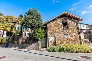 A stone building with a sloped roof, a metal gate, and a small window. - Casa Naima: Family House Terrace & Peaceful Location (Alto Malcantone)