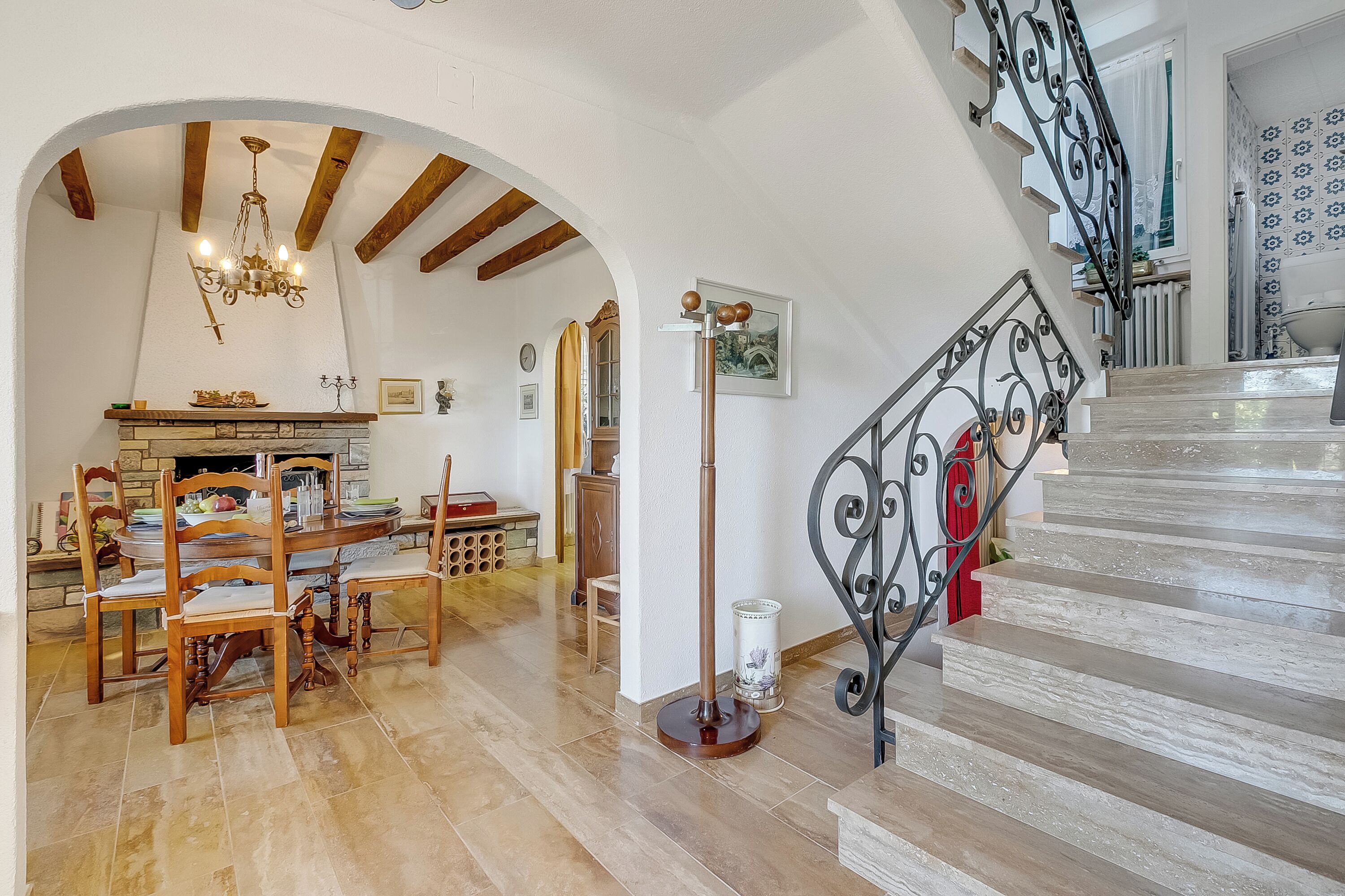 Un coin repas avec des chaises en bois et un lustre, un escalier avec une rampe en fer forgé, et une cheminée avec un manteau de cheminée.