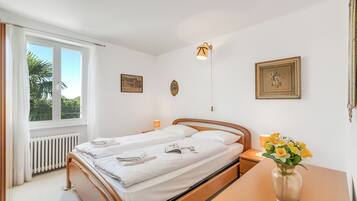 Un dormitorio con una cama, una mesita de noche, una lámpara, un florero con flores y dos cuadros en la pared.