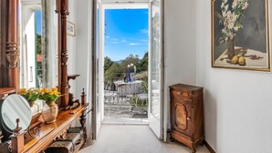 A corridor leading to an outdoor patio with a table and chairs, a wooden cabinet, and a painting on the wall. - Casa Naima: Family House Terrace & Peaceful Location (Alto Malcantone)