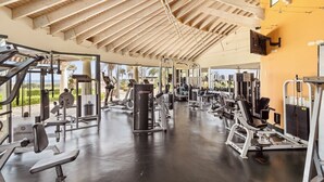 Een sportschool met diverse fitnessapparaten, een houten plafond en grote ramen.