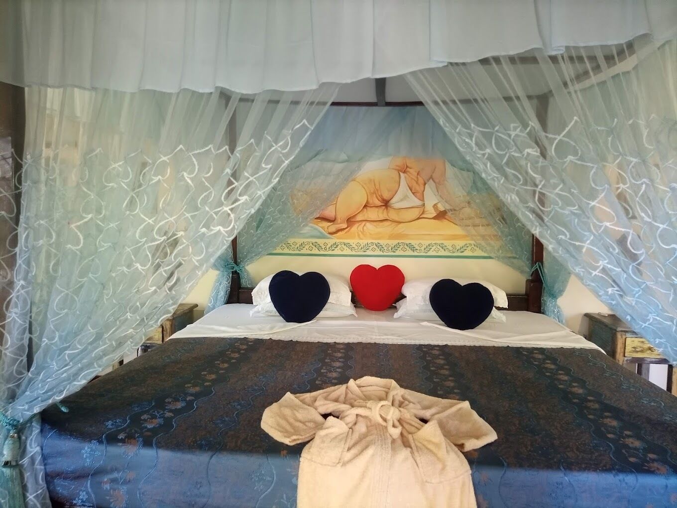 A bed with a canopy, a painting on the wall, and heart-shaped pillows.