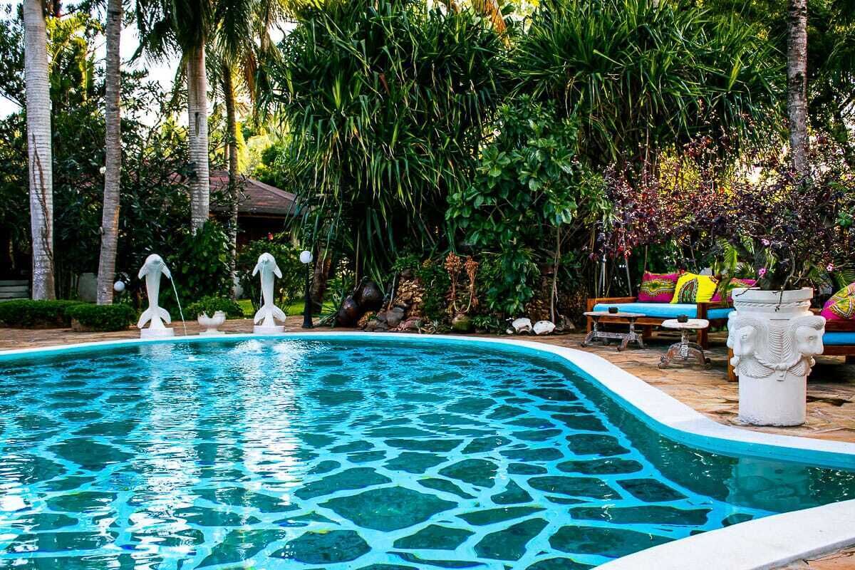 A swimming pool with a stone pattern, surrounded by lush greenery and a lounge area with colorful cushions.