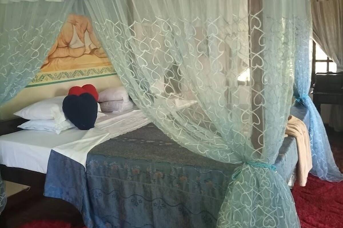 Una cama con dosel, un ventilador de techo y una ventana con cortinas.