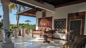 A spacious patio with a wooden bench, a round table, and a large painting of a lion. - African House Resort Malindi (Malindi)