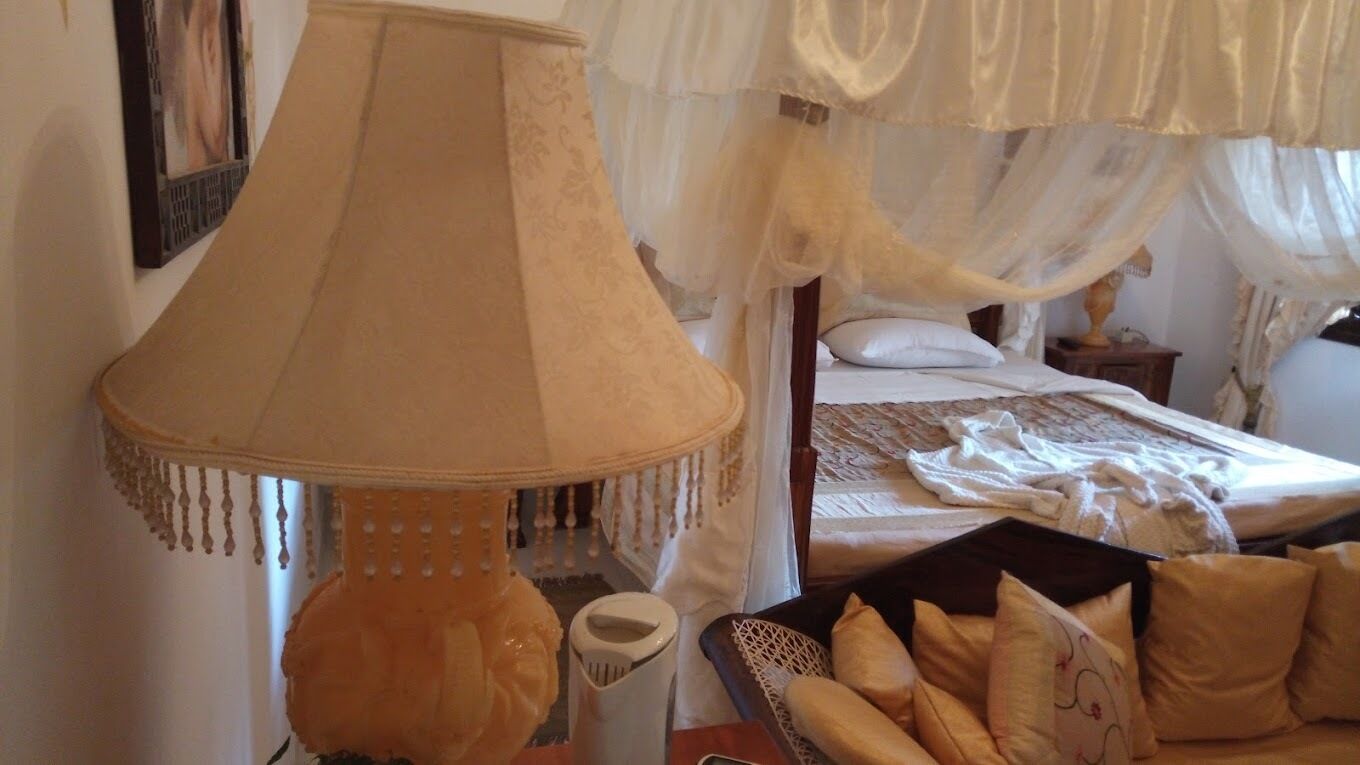 A bedroom with a bed, a bedside table, a lamp, and a basket of pillows.