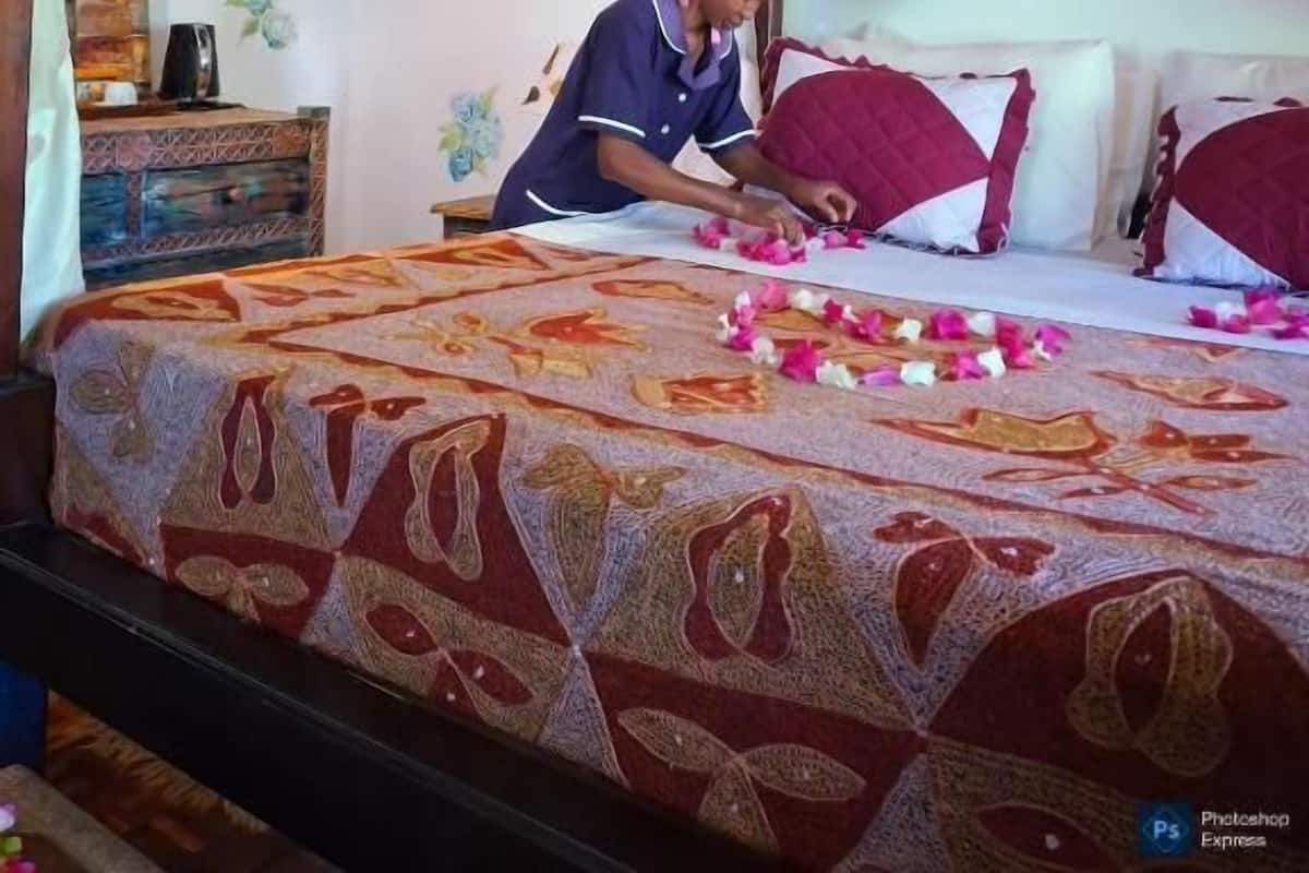 Una cama con una colcha estampada, un dosel y una persona arreglando flores sobre la cama.
