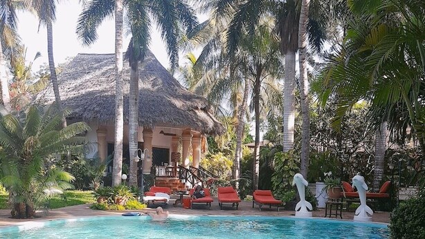 A swimming pool with lounge chairs and palm trees. - African House Resort Malindi (Malindi)