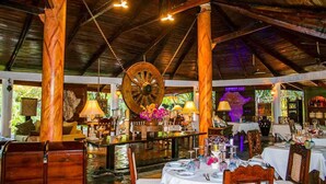 A restaurant with wooden beams, a large wooden wheel chandelier, and tables set for dining. - African House Resort Malindi (Malindi)