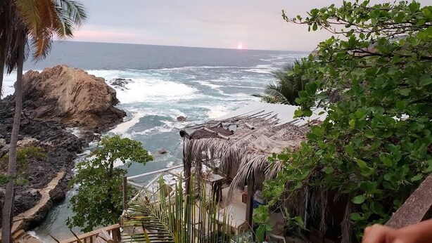 Un paysage côtier avec une rive rocheuse, une construction au toit de chaume et une végétation luxuriante.