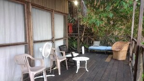 Un espace extérieur abrité, avec des chaises en plastique, une petite table ronde et un fauteuil en osier.