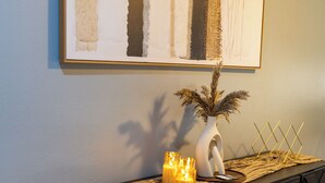 A modern living room with a dark console table, a white vase with dried plants, and a framed abstract painting on the wall. - Enjoy a stylish, comfort, space experience in this beautiful maintained home. (Baton Rouge)