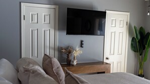 A bedroom with a bed, a TV mounted on the wall, a wooden nightstand, and a potted plant. - Enjoy a stylish, comfort, space experience in this beautiful maintained home. (Baton Rouge)