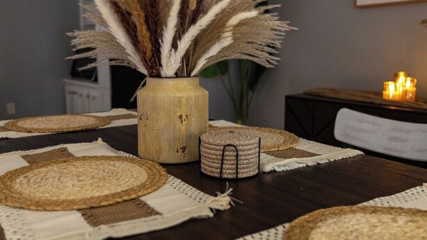 A dining table with woven placemats, a vase with dried pampas grass, and candles on a side table. - Enjoy a stylish, comfort, space experience in this beautiful maintained home. (Baton Rouge)