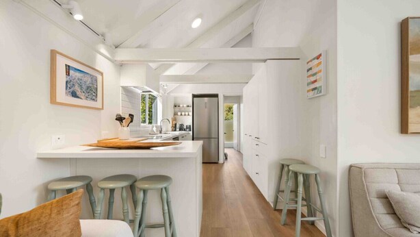 Una cocina moderna con una isla central, taburetes de bar y una zona de comedor con sofá.