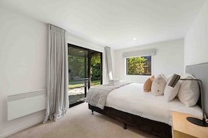 A bedroom with a large bed, a window with a view of greenery, and a sliding glass door leading to an outdoor area. - Lake & Mountain Views | 2 Living Areas | Sleeps 8 (Wānaka)