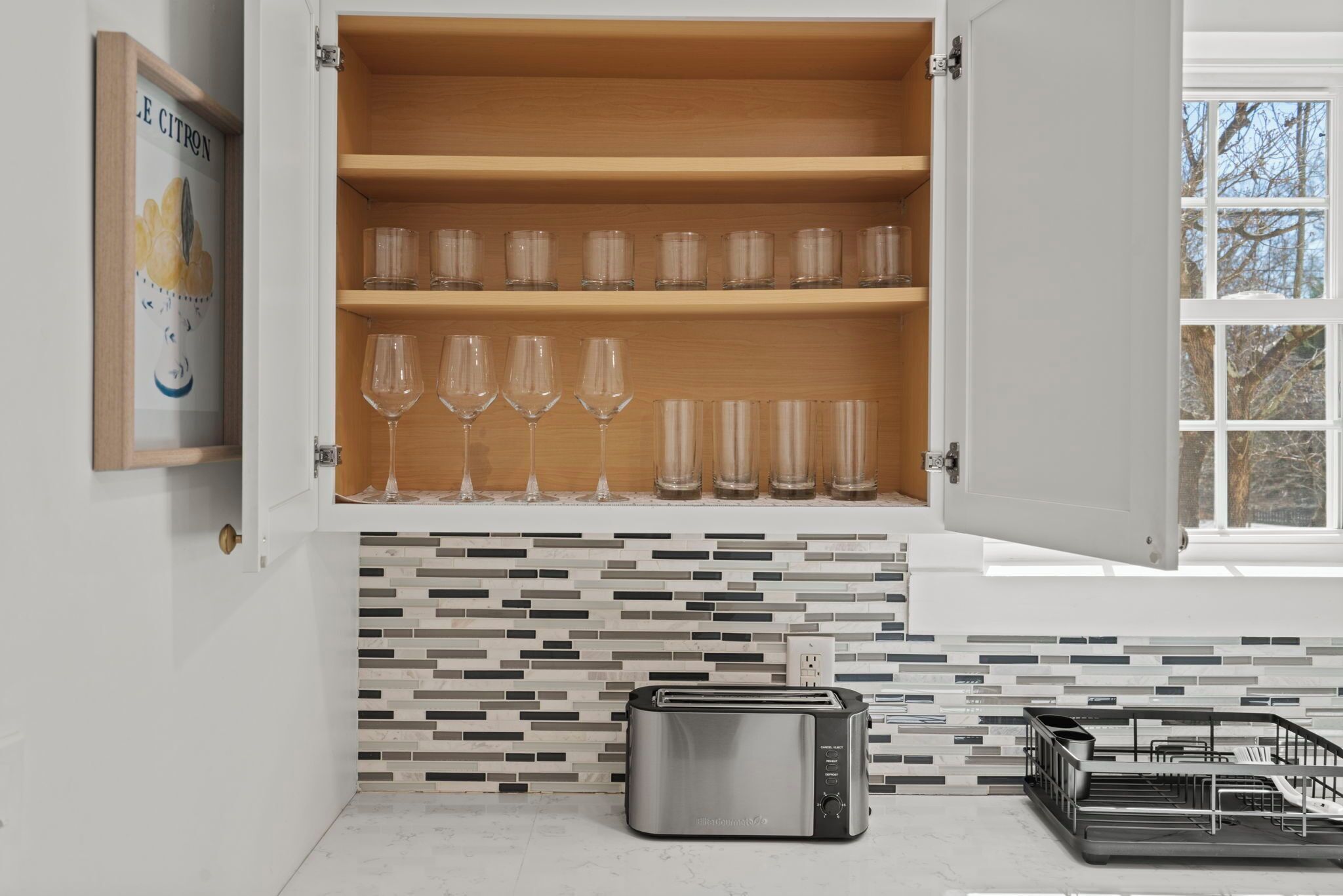 A kitchen with a toaster, a wine glass shelf, and a tiled backsplash.