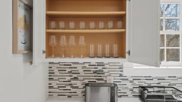 A kitchen with a toaster, a wine glass shelf, and a tiled backsplash.