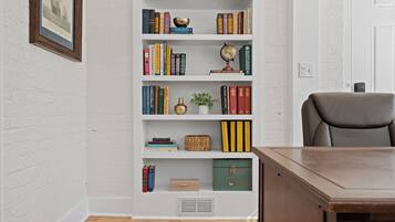 A room with a wooden desk, a bookshelf with various books and decorative items, a globe, and a framed picture on the wall.