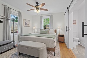 A bedroom with a bed, bedside tables, a bench, a ceiling fan, and a window with curtains.