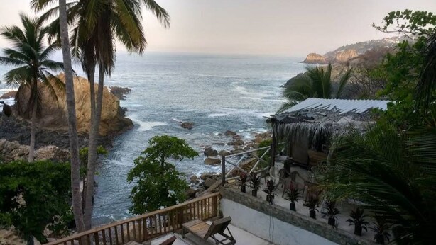 A pool area with lounge chairs, a view of the ocean, and a thatched-roof structure. - Villa Cocos (Acapulco de Juárez)