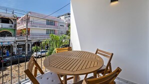 A balcony with a round wooden table and chairs, overlooking a street with buildings and parked cars. - Unit Pepinillo Romantic Zone (Puerto Vallarta)