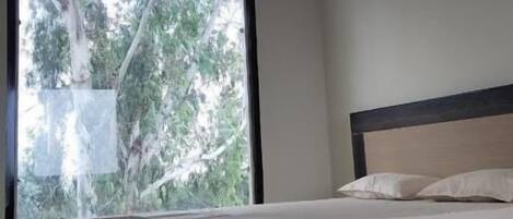 A bedroom with a bed, a ceiling fan, and a large window with a view of trees.