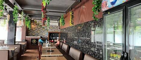 A restaurant interior with wooden tables, booths, hanging plants, and a Pepsi refrigerator.