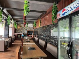 Egy étterem belső tere, melyben fából készült asztalok, különálló ülőfülkék, lógó növények és egy Pepsi hűtőszekrény található.