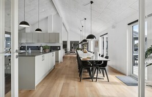 A modern kitchen with a central island, a dining area with a long table and chairs, and large windows allowing natural light. - Amazing home in Idestrup with sauna (Idestrup)