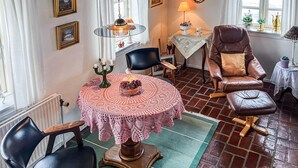 Un coin repas chaleureux avec une table ronde recouverte d’une nappe en dentelle, entourée de fauteuils en cuir. Un chandelier avec des bougies est posé sur la table, et un lustre est suspendu au-dessus.