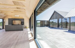 Une cuisine moderne dotée d’un grand îlot central, d’un coin repas avec une table et des chaises, et d’une grande baie vitrée donnant sur un patio.