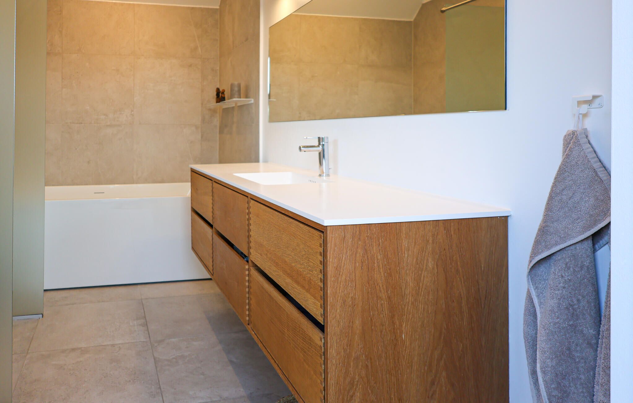 A modern bathroom with a wooden vanity, a white sink, and a large mirror.