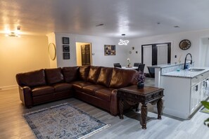 A living room with a brown leather sofa, a patterned rug, a dining table with chairs, and a kitchen area with a countertop and cabinets. - 3-bedroom house in peaceful San Antonio with cool AC (San Antonio)