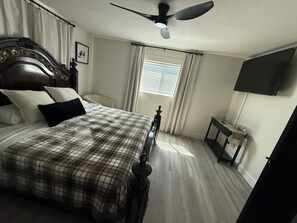 A bedroom with a large bed, a ceiling fan, a bedside table with a lamp, and a TV mounted on the wall. - 3-bedroom house in peaceful San Antonio with cool AC (San Antonio)