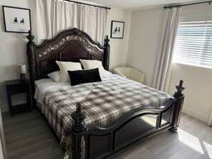 Ein ordentlich bezogenes Bett mit einer Karo-Decke, einem dunklen Holz-Kopfschild und zwei weißen Kissen.